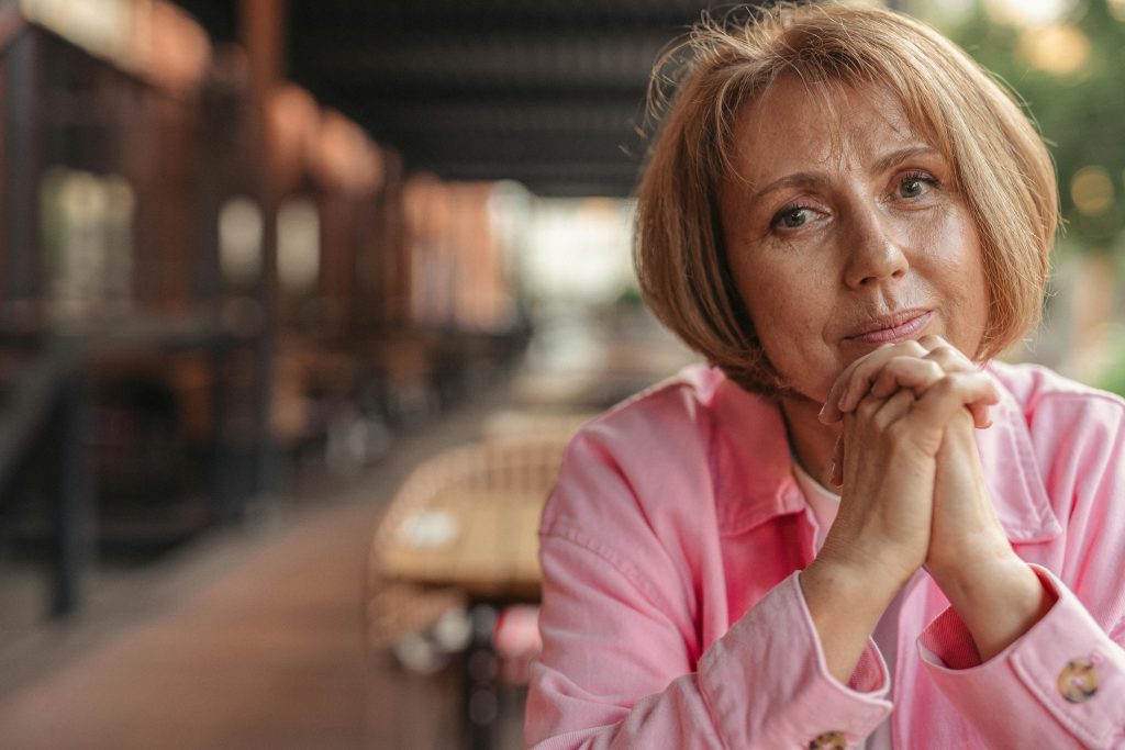 Charming senior woman with hands clasped enjoys a peaceful moment outside.